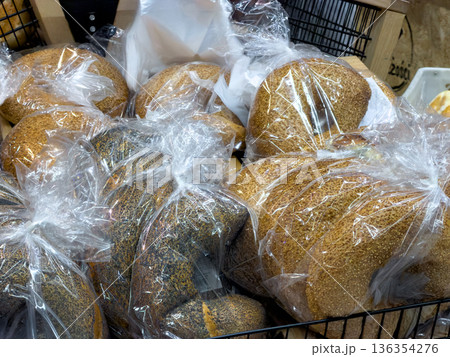 Artisanal freshly baked bread loaves, topped with sesame and poppy seeds, individually wrapped in clear plastic bags for hygienic supermarket retail display Artisanal freshly baked bread loaves, topped with sesame and poppy seeds, individually wrapped in clear plastic bags for hygienic supermarket retail display 136354276