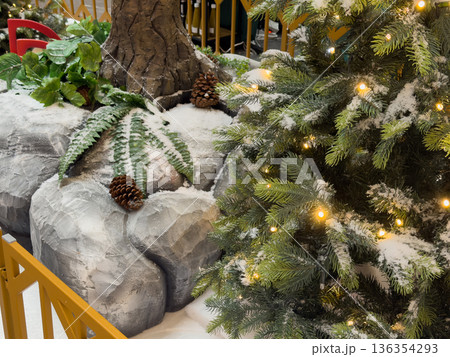 Illuminated artificial Christmas tree featuring snow-dusted branches, warm lights, pinecones, and frosted rocks, creating a beautiful winter holiday display Illuminated artificial Christmas tree featuring snow-dusted branches, warm lights, pinecones, and frosted rocks, creating a beautiful winter holiday display 136354293