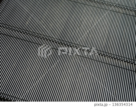 Close-up of moving escalator steps showcasing metallic parallel lines forming a dynamic abstract pattern for modern design, urban infrastructure, and transportation 136354314