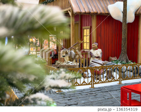 Detailed Christmas display featuring a charming red house, festive reindeer statue, and a cozy Santa figure, creating a joyful holiday shopping atmosphere in a retail mall 136354319