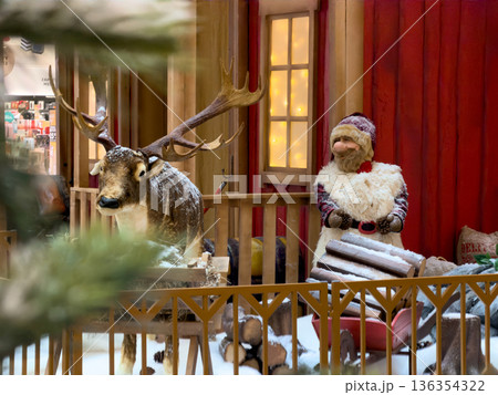 Charming festive display with a majestic reindeer and whimsical Santa Claus figure in a snowy, rustic cabin scene, evoking joyful Christmas spirit 136354322
