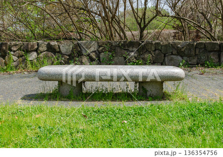 公園の木陰に佇む石造りのベンチ 136354756