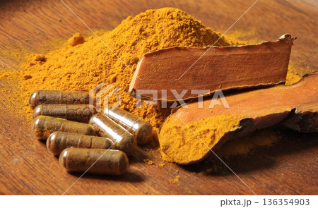 Turmeric powder, turmeric rhizomes, and turmeric capsules in a bowl. 136354903