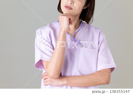 悩む医療用スクラブ姿のミドル女性看護師 136355147