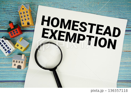 Notepad with "Homestead Exemption" with magnifying glass and house model on wooden background 136357118