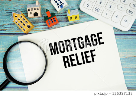 Notepad with "Mortgage Relief" with Calculator, magnifying glass and house model on wooden background 136357135