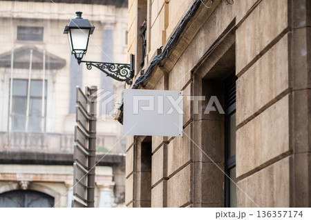 Blank white signage mock-up on a classic stone building facade, showcasing a traditional wrought iron street lamp, offering clear space for branding and messaging in an urban setting 136357174