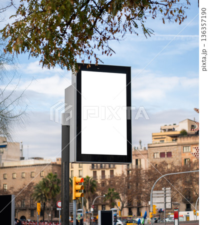 Vertical blank street billboard mockup with digital display and copy space for outdoor marketing along a Barcelona city street, framed by buildings, traffic light and sky 136357190