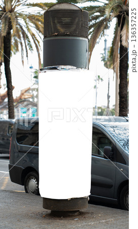 Blank advertising column mockup standing on a city street pavement with parked minivans and palm trees in the background, creating a perfect space for outdoor media marketing 136357225