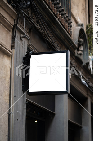 Blank square sign providing space for branding, advertising, or information, mounted to an old urban building facade with visible wires and architectural details 136357229