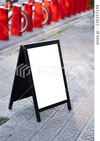 Blank A-frame sidewalk sign on patterned pavement offering clear customizable space for menus, promotions or branding in an urban street scene with blurred city background 136357249
