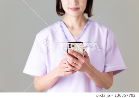 スマホを持つ医療用スクラブ姿のミドル女性看護師 136357702