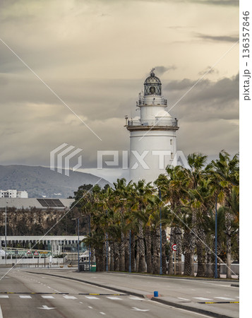 White Lighthouse Over Coastal Road Framed by Palm Trees Under Cloudy Sky Near Harbor White Lighthouse Over Coastal Road Framed by Palm Trees Under Cloudy Sky Near Harbor 136357846