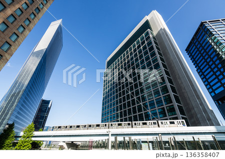 Low-angle view of a New Transit Yurikamome line train running on the elevated track with modern skyscrapers in Shiodome, Minato, Tokyo, Japan. It's an automated guideway transit service in Tokyo. 136358407