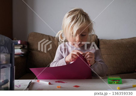 Little girl crafting at home, cutting paper and drawing at the table 136359330