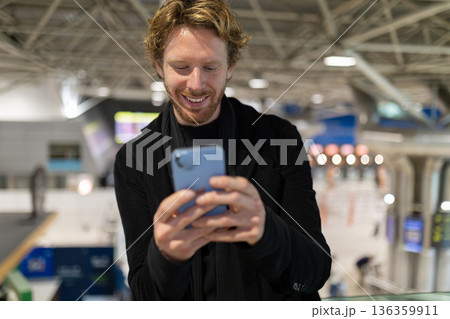 Young man smiling using smartphone at transport hub 136359911