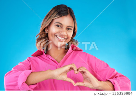 Woman, heart shape and smile portrait in studio for love, fashion or happiness. Happy person show sign with hands, icon or emoji for support, kindness and motivation for charity on a blue background 136359994