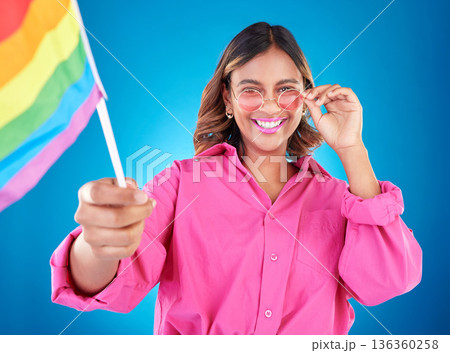 Woman, lgbtq and pride flag in studio portrait, sunglasses or icon with smile for human rights by blue background. Gen z girl, young lesbian student and wave sign for solidarity, freedom or inclusion Woman, lgbtq and pride flag in studio portrait, sunglasses or icon with smile for human rights by blue background. Gen z girl, young lesbian student and wave sign for solidarity, freedom or inclusion 136360258