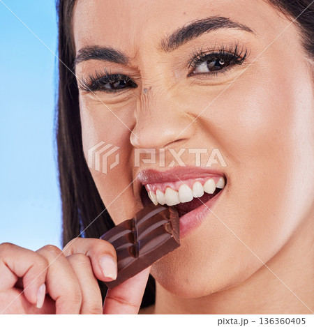 Chocolate, happy and portrait of woman in studio eating luxury, sweet treats and candy on blue background. Sugar, unhealthy diet and face of female person with cocoa bar, dessert and delicious snack 136360405