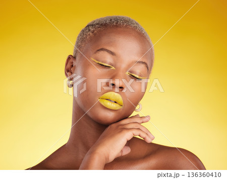 Face, makeup and lipstick with a black woman in studio on a yellow background for creative, beauty or cosmetics. Gold, color and eyeshadow on young model with eyes closed for fashion or aesthetic Face, makeup and lipstick with a black woman in studio on a yellow background for creative, beauty or cosmetics. Gold, color and eyeshadow on young model with eyes closed for fashion or aesthetic 136360410
