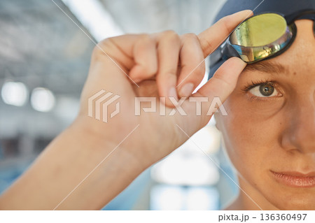 Sports, eye and goggles with a woman swimmer getting ready for an event, race or competition in a gym. Fitness, exercise and workout with the face a young athlete training at a swimming pool closeup 136360497