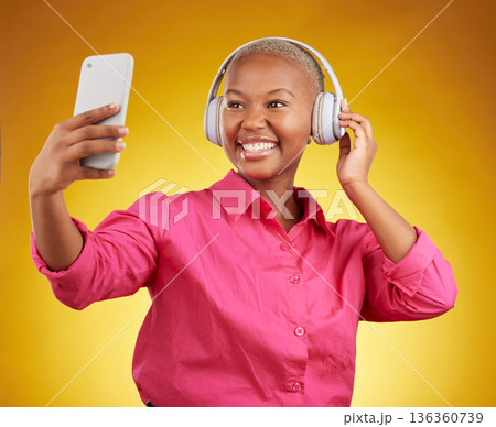 Smile, selfie and black woman with headphones for music, radio and podcast in studio isolated on a yellow background. Profile picture, photographer and African person or influencer on social media Smile, selfie and black woman with headphones for music, radio and podcast in studio isolated on a yellow background. Profile picture, photographer and African person or influencer on social media 136360739