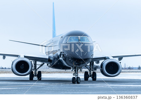 Close-up front view of a black passenger airplane taxiing at winter airport Close-up front view of a black passenger airplane taxiing at winter airport 136360837
