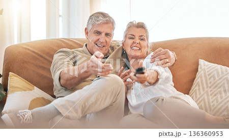 Happy senior couple, watching tv and sofa in relax for streaming, movie or series in living room at home. Portrait of elderly man and woman smile with remote for changing channel and entertainment Happy senior couple, watching tv and sofa in relax for streaming, movie or series in living room at home. Portrait of elderly man and woman smile with remote for changing channel and entertainment 136360953