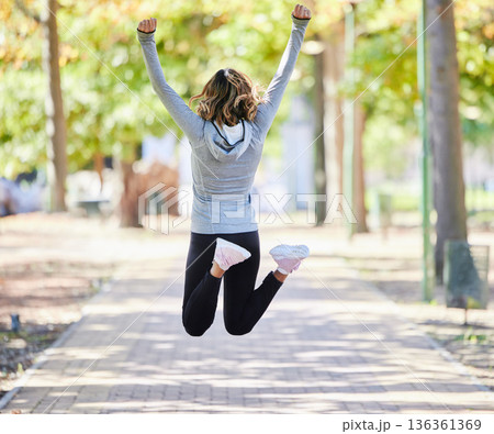 Fitness, jump and a woman outdoor for success at a park to celebrate win or achievement. Back of young female person on a road in nature excited about workout, running or training goals or freedom 136361369