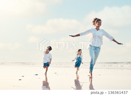 Mother, son and daughter on the beach to dance together while outdoor for travel or vacation in summer. Sunset, family or children and a woman having fun with her kids on the coast by the ocean 136361437