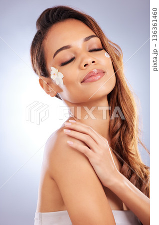 Skincare, woman with flower and cream on face, natural makeup and spa treatment on white background. Dermatology, beauty and glow, model with floral lotion and organic facial cosmetics in studio. 136361460