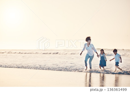 Playing, mother and children at beach on a fun family vacation, holiday or nature adventure at sunset. Young boy and girl holding hands with a woman outdoor for fun energy, happiness and banner space 136361499