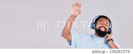 Headphones, mockup and young man in a studio listening to music, playlist or album while dancing. Happy, smile and African male model streaming a song or radio by a gray background with mock up space 136361574