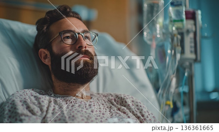 Patient man in hospital bed, beard, glasses. IV drips nearby. Medical care. Patient man in hospital bed, beard, glasses. IV drips nearby. Medical care. 136361665