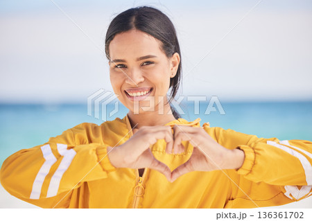 Happy woman, portrait and heart hands on beach for love, care or support in trust, health or romance. Outdoor female person with emoji, symbol or icon for like or wellness in peace, sign or emoticon 136361702