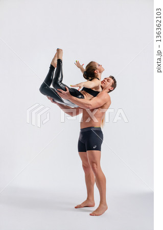 Strong man lifting graceful woman in a dynamic acrobatic pose in a studio. Strong man lifting graceful woman in a dynamic acrobatic pose in a studio. 136362103