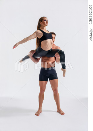 Strong man lifting a graceful woman in an acrobatic dance pose. Couple demonstrating balance and partnership against a white background. Strong man lifting a graceful woman in an acrobatic dance pose. Couple demonstrating balance and partnership against a white background. 136362106