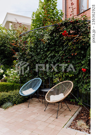 Cozy patio corner with two lounge chairs and roses on trellis in lush garden 136362928