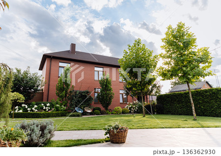 Sunlit backyard lawn with brick house and manicured landscaping 136362930