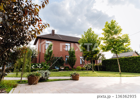 Brick family house with landscaped backyard, green lawn, trees and patio in sunlight Brick family house with landscaped backyard, green lawn, trees and patio in sunlight 136362935