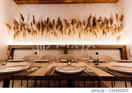 Cozy restaurant table set with pampas grass wall decor and warm ambient light Cozy restaurant table set with pampas grass wall decor and warm ambient light 136362977