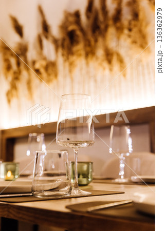 Elegant restaurant table with wine glasses, candles and pampas grass backdrop 136362979
