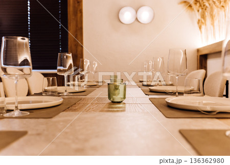 Elegant long dining table set with wine glasses and warm ambient light 136362980