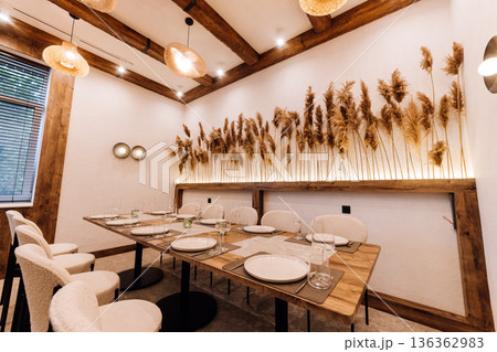 Cozy boho private dining room with pampas wall, set table and rattan lights 136362983