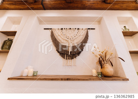 Boho macrame wall hanging with candles and dried flowers on rustic shelf 136362985