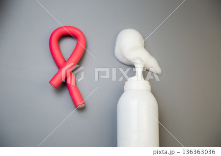 A close-up on a gray background shows a bottle of foam for long-term hair styling, white foam poured out of it, next to it lies a curved pink curler. The concept of styling, hairstyle, curls. High 136363036