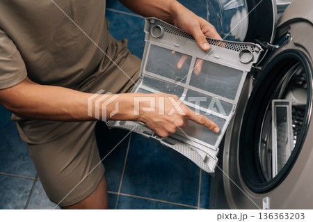 Person removing lint from tumble dryer filter, performing routine household chore and essential appliance maintenance, ensuring proper functioning and preventing fire hazards. 136363203