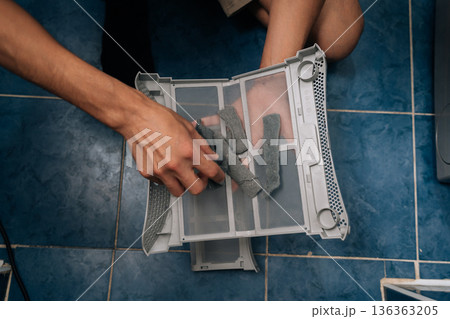 Top view of hands cleaning accumulated lint from dryer filter, demonstrating routine household chore and essential appliance maintenance for optimal performance and preventing fire hazards. 136363205