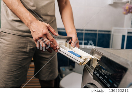 Cropped shot of man opening washing machine detergent dispenser drawer in the bathroom, pulling out the compartment to add laundry detergent for washing clothes. 136363211