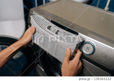 Man removing lint filter from modern tumble dryer, performing routine appliance maintenance for optimal performance and household safety, preventing fire hazards and improving laundry efficiency. 136363222